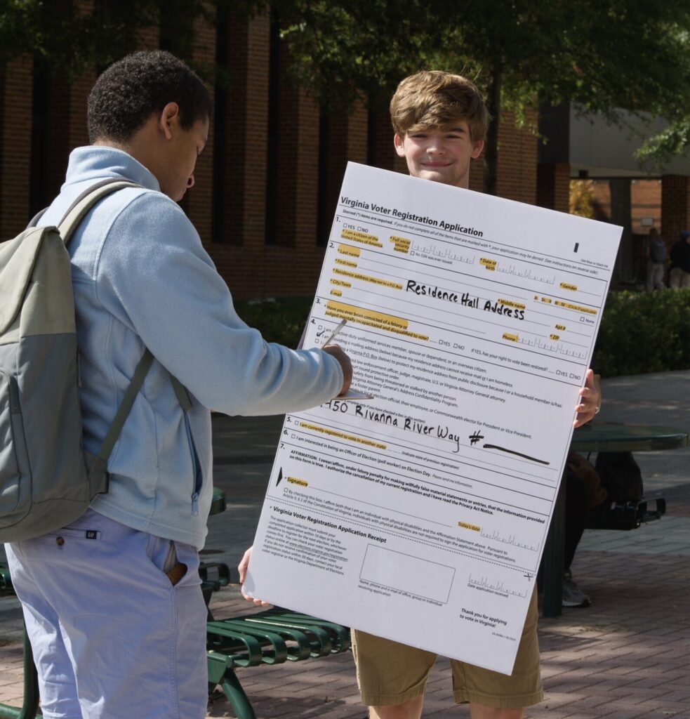 A person references an enlarged version of the Virginia Voter Registration Application as he completes his own voter registration form