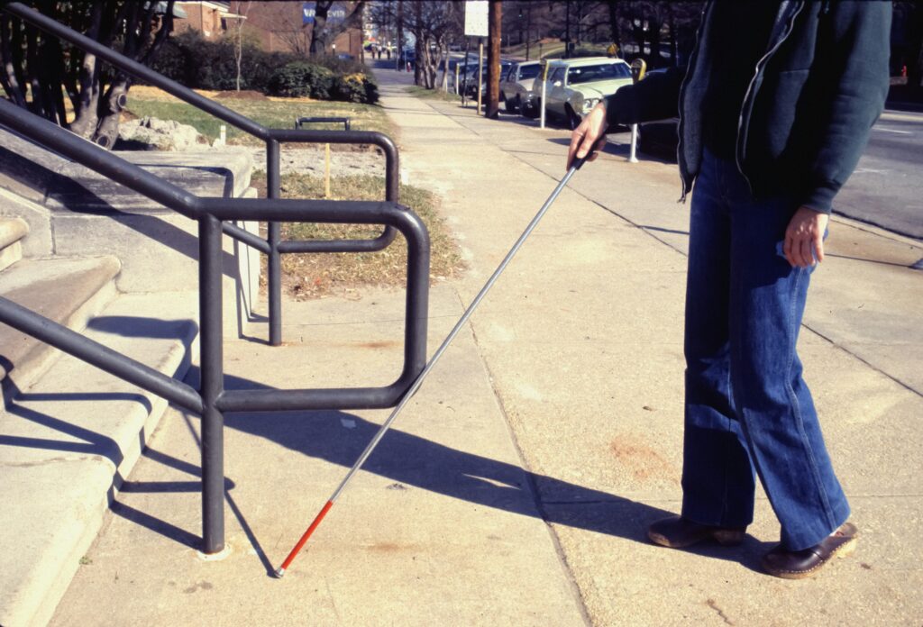A blind person using a cane walks toward steps