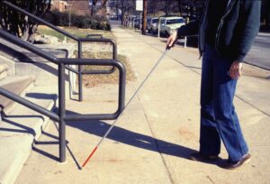 A blind person using a cane walks toward steps