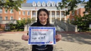 A young woman holds a sign with the words "I vote because Judy Heumann fought for me!"